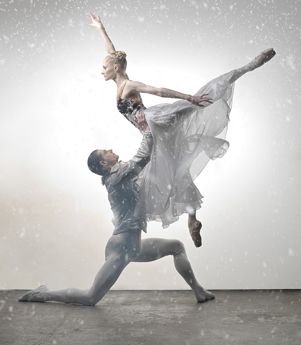 Image of a male and female ballet dancer on stage, he male dancer kneeing on one knee and holding the female ballerina aloft.